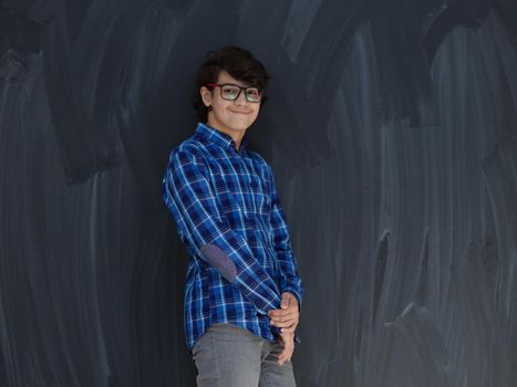 portrait  of smart looking arab teenager with glasses wearing a hat in casual school look against black chalkboard background