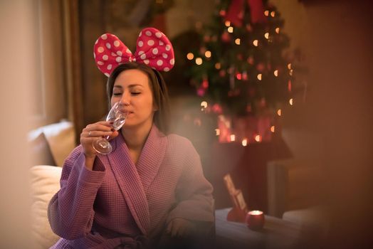 people, and relaxation concept   beautiful young woman in bath robe drinking champagne at spa over holidays lights background