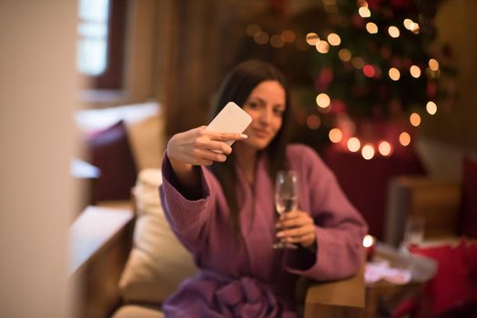 people, and relaxation concept   beautiful young woman in bath robe drinking champagne and doing selfy at spa over holidays lights background