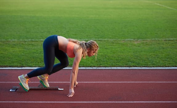 woman  sprinter leaving starting blocks on the athletic  track. Side view. exploding start