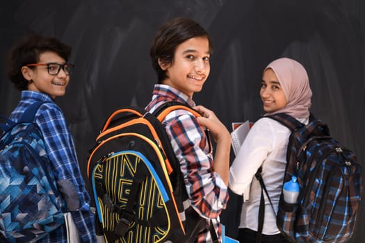 Arabic teenagers, students group portrait against black chalkboard wearing backpack and books in school.Selective focus. High quality photo