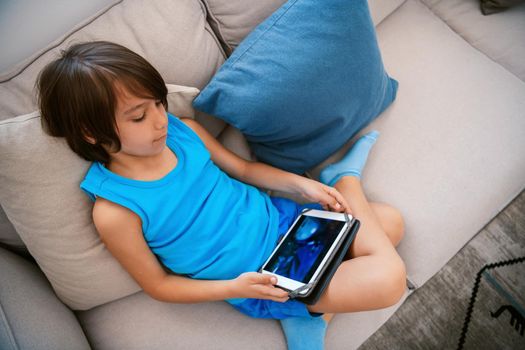 an Arab boy sits on the couch and uses a tablet for fun. High quality photo