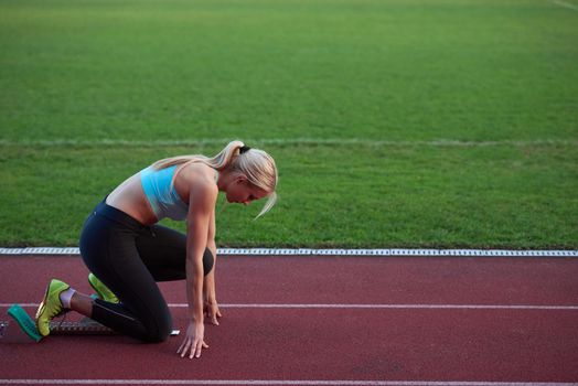 woman  sprinter leaving starting blocks on the athletic  track. Side view. exploding start