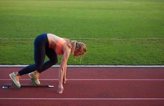 woman  sprinter leaving starting blocks on the athletic  track. Side view. exploding start