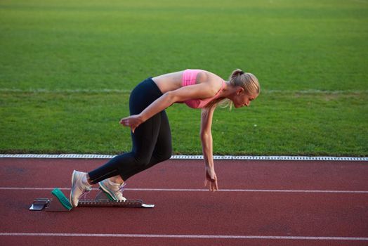 woman  sprinter leaving starting blocks on the athletic  track. Side view. exploding start