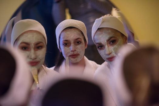 a group of young beautiful women looking in the mirror while putting face masks in the bathroom