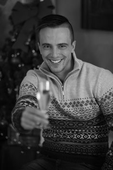 Portrait of a happy young man with a glass of champagne celebrating winter holidays at home beautifully decorated for Christmas