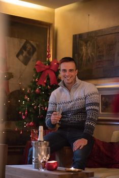 Portrait of a happy young man with a glass of champagne celebrating winter holidays at home beautifully decorated for Christmas