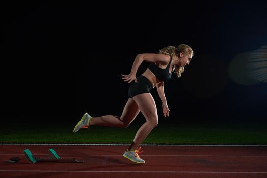 woman  sprinter leaving starting blocks on the athletic  track. Side view. exploding start