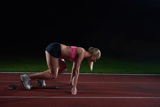 woman  sprinter leaving starting blocks on the athletic  track. Side view. exploding start