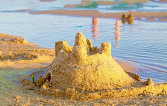 Beautiful sand castle illuminated by the morning sun on the beach of the tropical sea. The concept of a family vacation at sea.