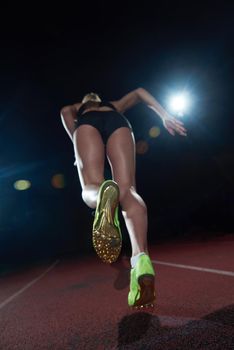 woman  sprinter leaving starting blocks on the athletic  track. Side view. exploding start