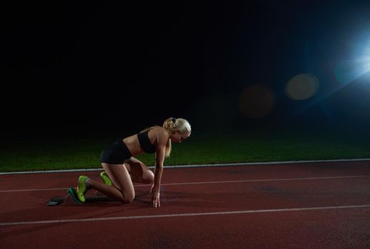 woman  sprinter leaving starting blocks on the athletic  track. Side view. exploding start