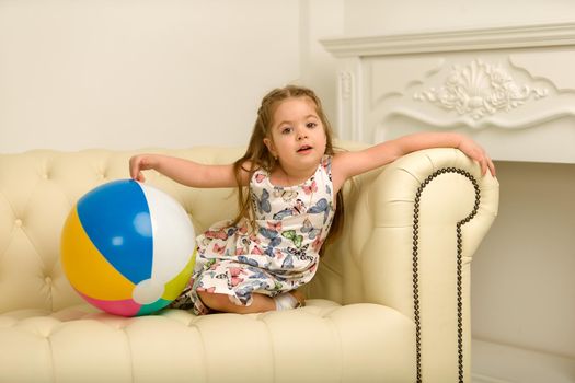 Adorable little girl playing with a ball on the sofa. Concept for family, advertising, happy childhood.