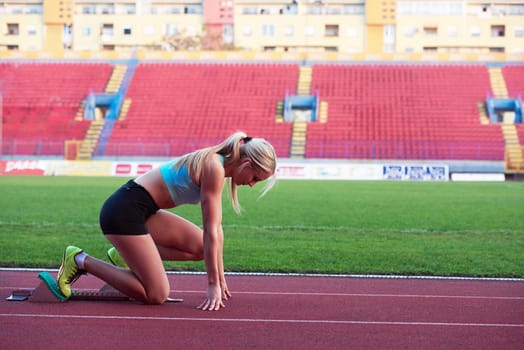 woman  sprinter leaving starting blocks on the athletic  track. Side view. exploding start