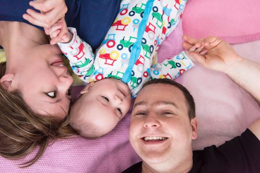 Top view of smiling young couple lying together with their adorable baby boy on blankets in their living room at home