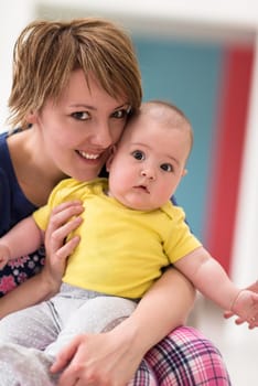 Portrait of young happy mother holding newborn baby boy while sitting on the sofa at home