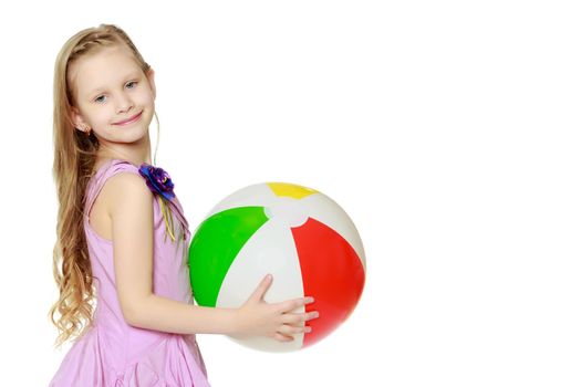 Happy little blond girl, with long curly hair, in a beautiful pink dress above the knees.She plays with a large multi-colored inflatable ball.