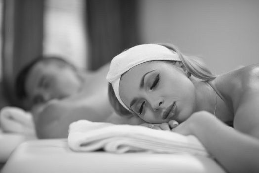 Portrait of relaxed beautiful young couple lying on massage table at spa center