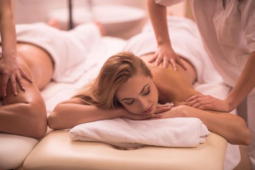 Relaxed young beautiful couple receiving a back massage from masseur in a spa