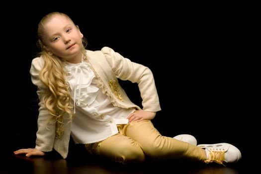 Beautiful little girl sitting in the studio on the floor on a black background. The concept of style and fashion.