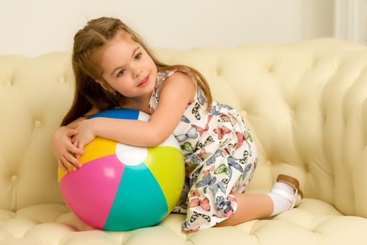 Adorable little girl playing with a ball on the sofa. Concept for family, advertising, happy childhood.