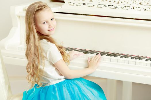 Caucasian little girl with long blond hair, in a beautiful pink skirt and white T-shirt and a pink bow on her chest.She plays music with the piano.