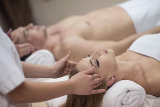 happy young beautiful couple enjoying head massage at the spa