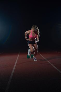 woman  sprinter leaving starting blocks on the athletic  track. Side view. exploding start