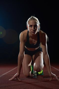 woman  sprinter leaving starting blocks on the athletic  track. Side view. exploding start