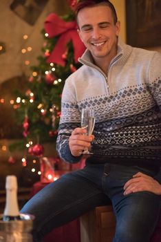 Portrait of a happy young man with a glass of champagne celebrating winter holidays at home beautifully decorated for Christmas