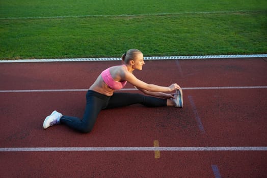 young runner sporty woman relaxing and stretching on athletic race track