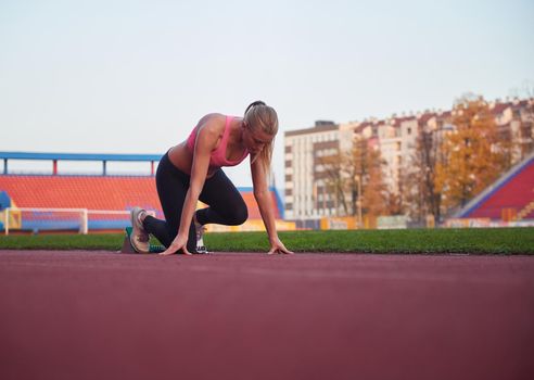 woman  sprinter leaving starting blocks on the athletic  track. Side view. exploding start