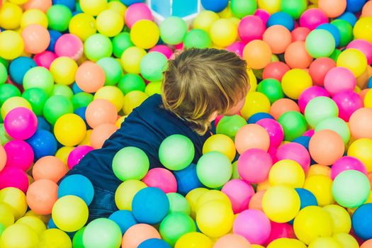 Happy little kid boy playing at colorful plastic balls playground high view. Funny child having fun indoors.