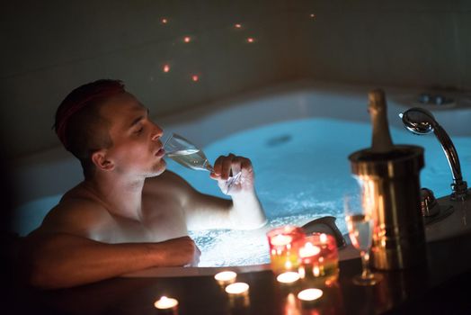 young handsome man enjoys relaxing in the jacuzzi with candles and champagne at luxury resort spa