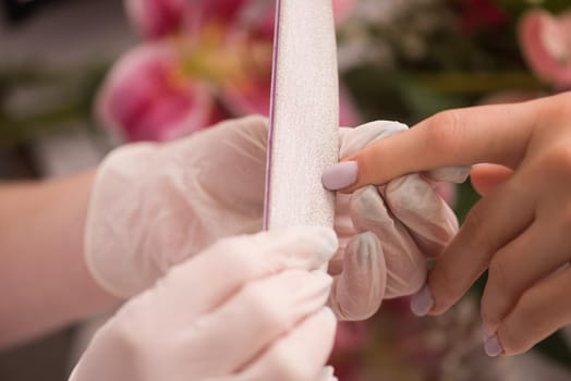 Woman hands receiving a manicure in beauty salon. Nail filing. Close up, selective focus.