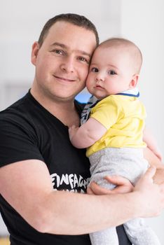 portrait of happy young father holding newborn baby boy near the window at home