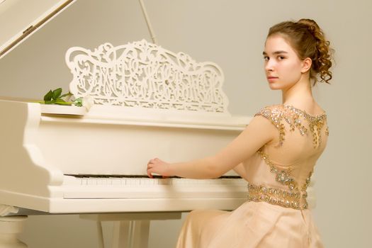 A teenage girl is playing on a white grand piano. The concept of creative development of personality, music education.