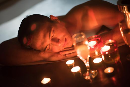 young handsome man enjoys relaxing in the jacuzzi with candles and champagne at luxury resort spa