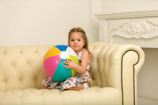 Adorable little girl playing with a ball on the sofa. Concept for family, advertising, happy childhood.