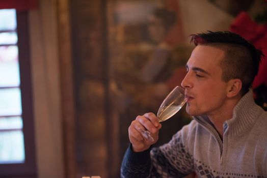 Portrait of a happy young man with a glass of champagne celebrating winter holidays at home beautifully decorated for Christmas