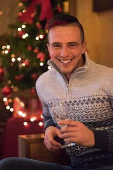 Portrait of a happy young man with a glass of champagne celebrating winter holidays at home beautifully decorated for Christmas