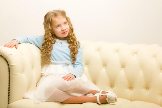 Little girl is sitting on the couch in the room. The concept of a happy childhood.