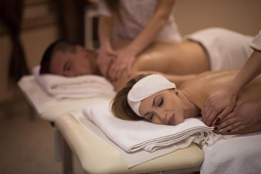 Relaxed young beautiful couple receiving a back massage from masseur in a spa