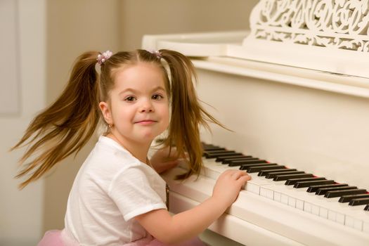 A nice little girl is playing on a big white piano. The concept of musical and aesthetic education of a child.