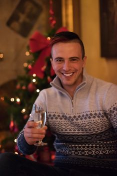 Portrait of a happy young man with a glass of champagne celebrating winter holidays at home beautifully decorated for Christmas