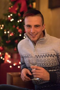 Portrait of a happy young man with a glass of champagne celebrating winter holidays at home beautifully decorated for Christmas