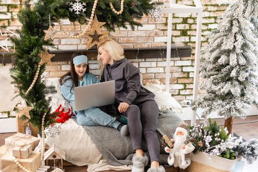 Caucasian woman with her daughter at christmas, having video chat with friends and family on laptop screen, sitting on sofa at home embracing. social distancing during covid 19 pandemic at christmas