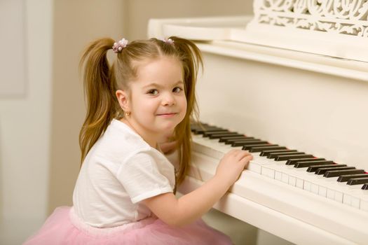 A nice little girl is playing on a big white piano. The concept of musical and aesthetic education of a child.