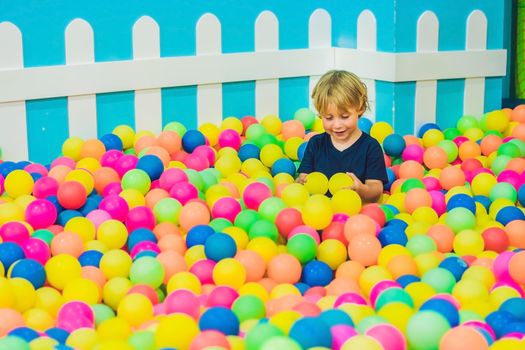 Happy little kid boy playing at colorful plastic balls playground high view. Funny child having fun indoors.